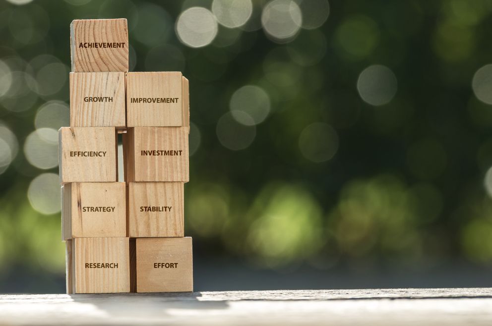 Image of small, wooden blocks with motivational words on them. In the background, is a blurred out green bush.