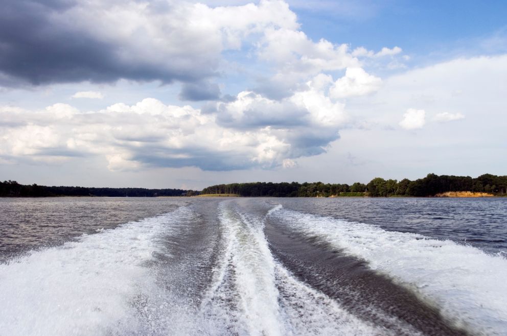 Image of wakes, most likely from a boat, and in the distance are trees.