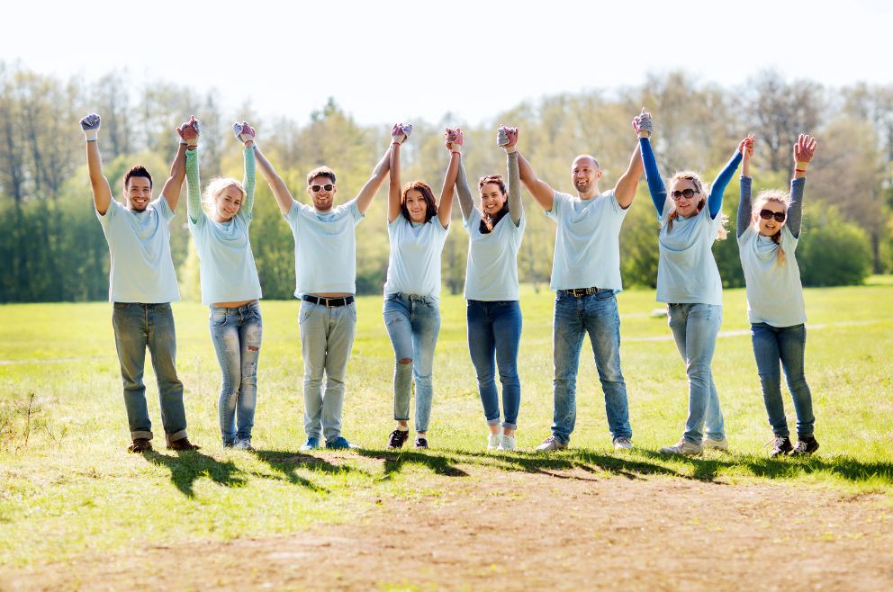Picture of eight happy people celebrating by holding hands together up in the air.