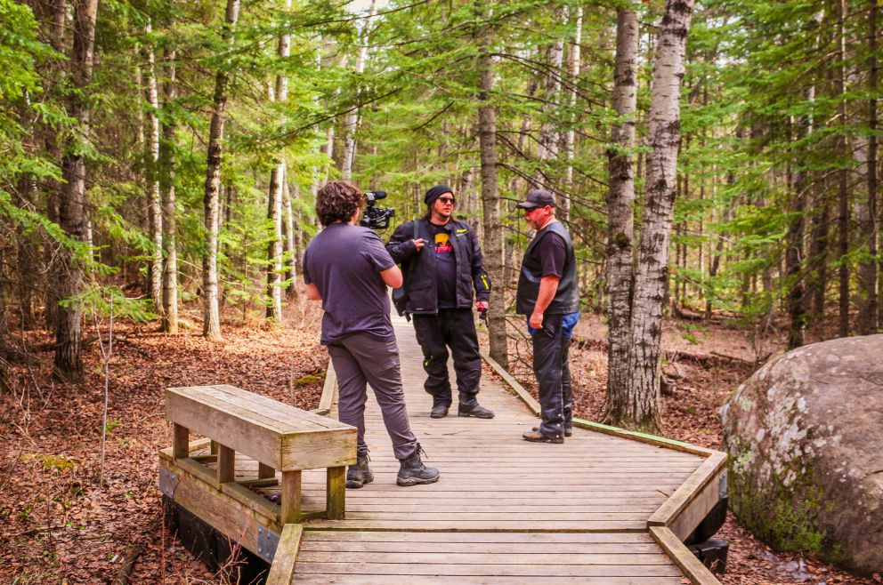 Epic Rides MB film crew standing on a board walk in the forest.