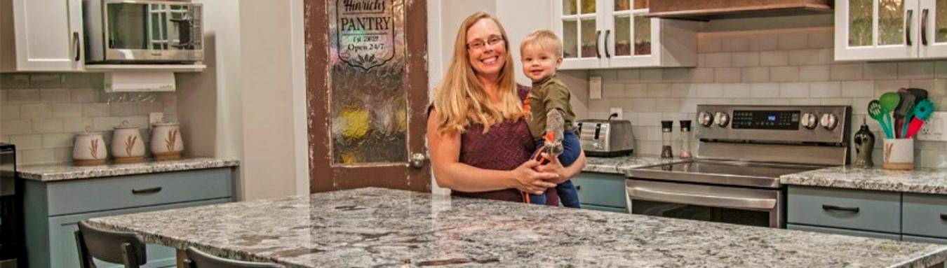 Photo of a woman holding a child while smiling at the camera in the kitchen with Granite Mountain's countertops.