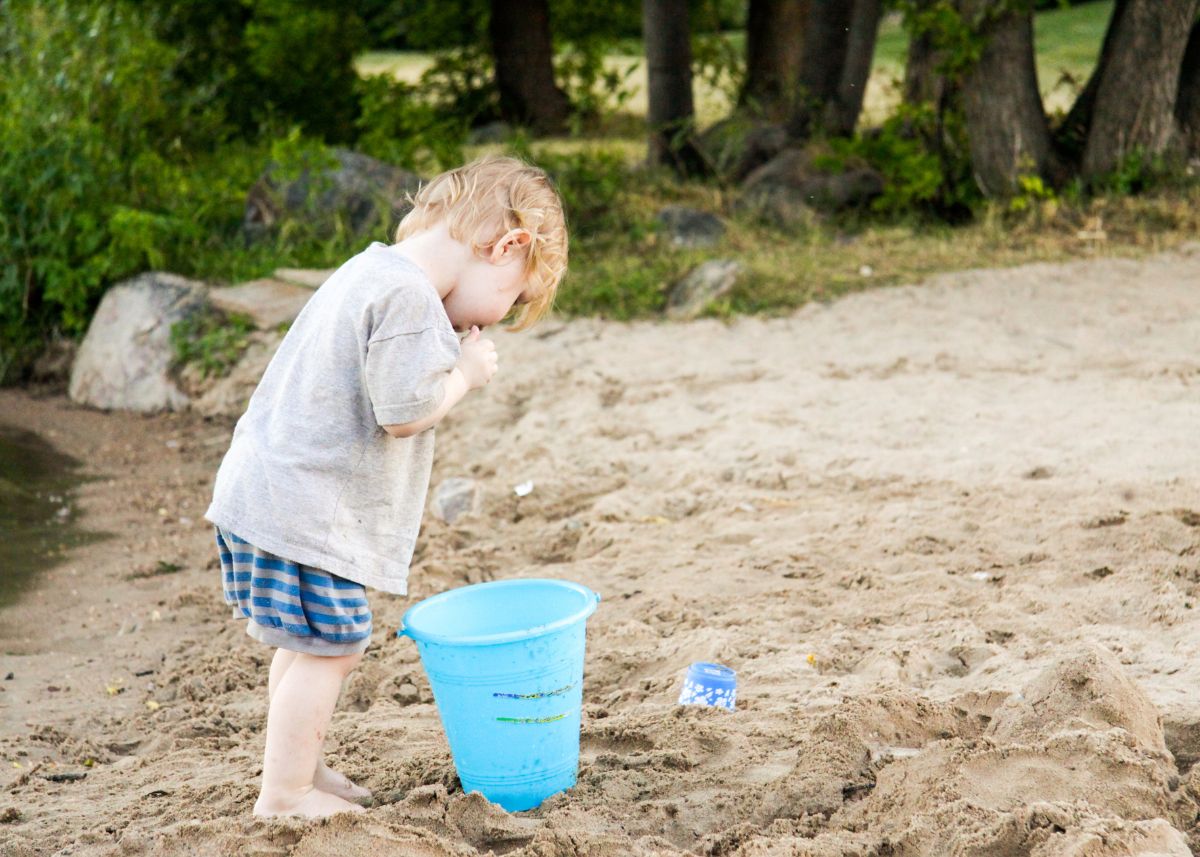 Toddler filling a pail with sand at the Lac du Bonnet Beach.
