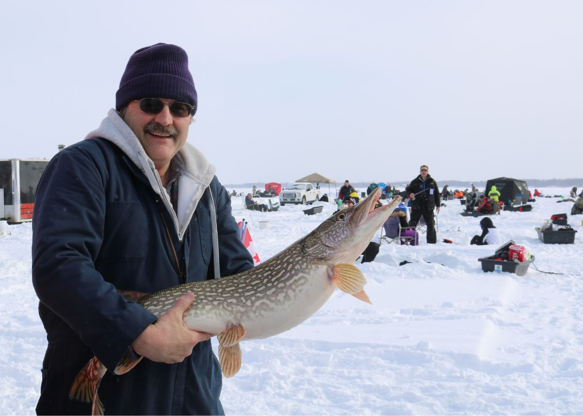 Man holding a master pike he pulled up during the Lac du Bonnet Ice Fishing Derby