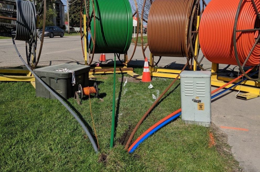 Fiber optic cables being fed into the ground from a large spool.