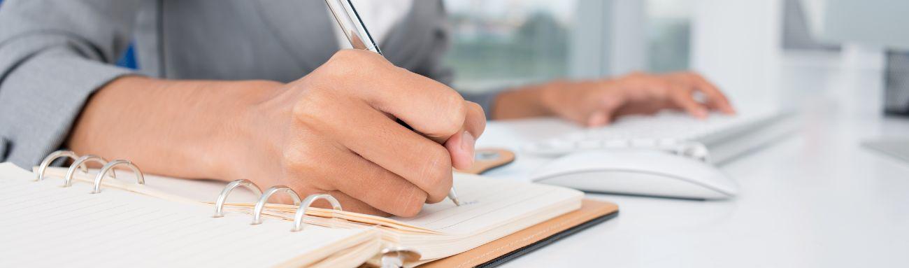 Photo shows an Administrative Assistant writing in a notebook.