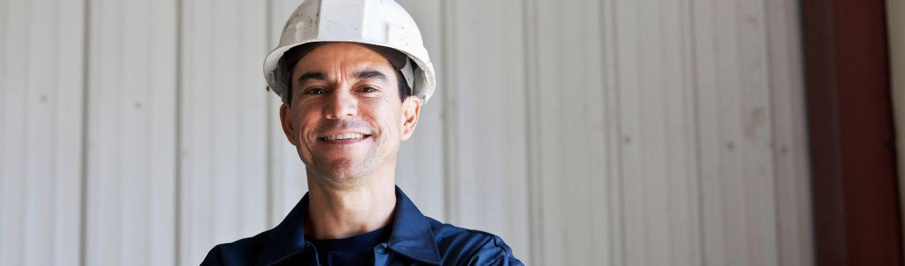 Photo shows a man smiling while wearing a white hard hat.